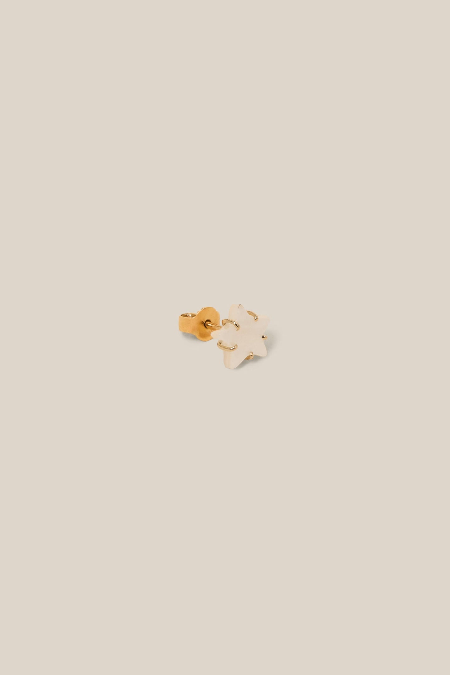 Small gold and white earring on a beige background