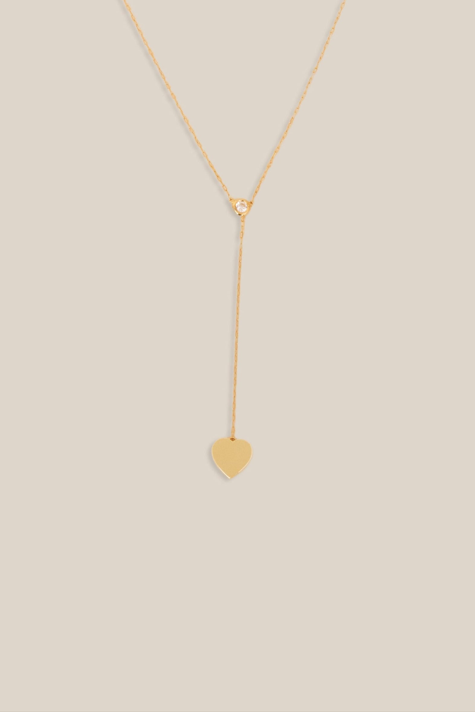 Gold necklace with a heart pendant on a beige background