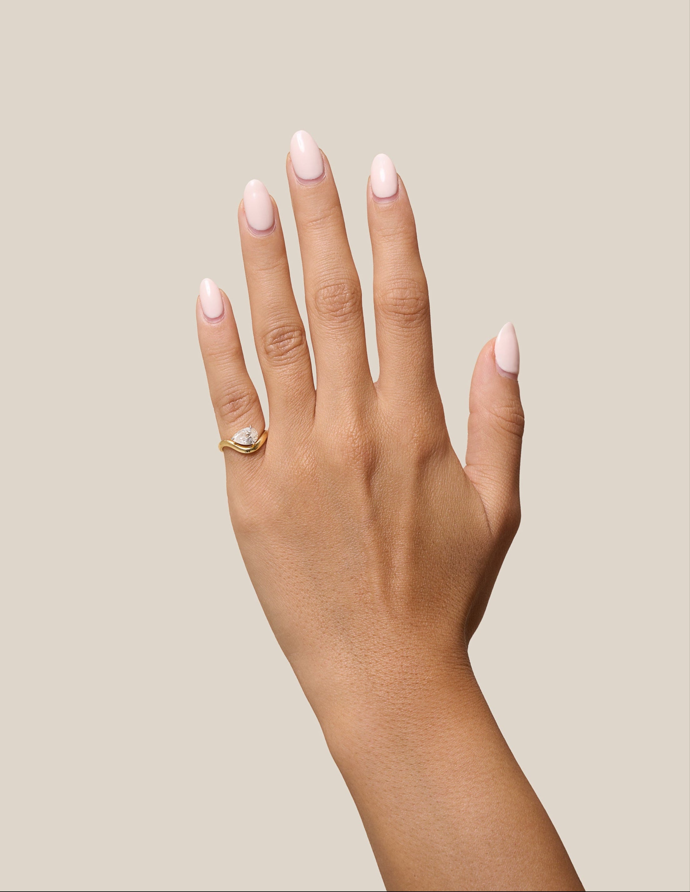 Hand with pink nail polish and a gold ring on a beige background