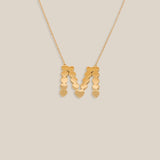 Gold necklace with a 'M' pendant on a beige background