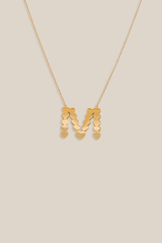 Gold necklace with a 'M' pendant on a beige background